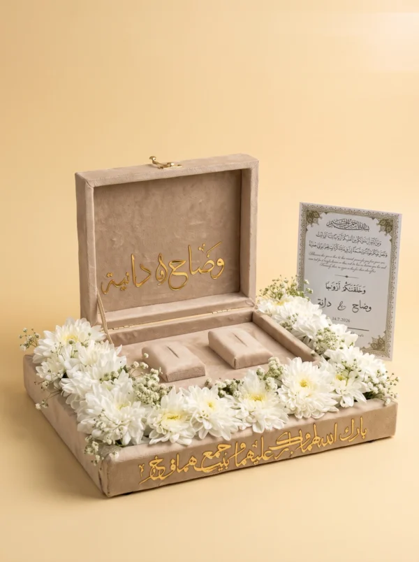 Velvet ring box with gold names in white flowers beside a framed wedding verse card with the couple's date