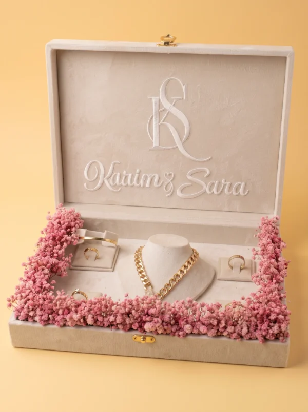 Cream velvet box with white monogram, first names, necklace and rings in a gypsophila wreath