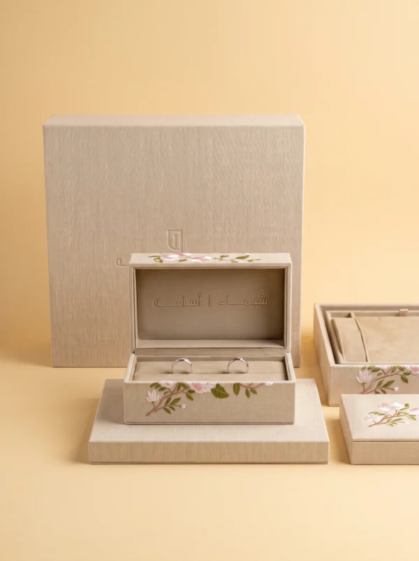 Linen ring box with Arabic names debossed in the lid, shown with its outer case and matching boxes